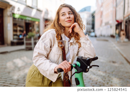 Happy woman rides an electric scooter in the city street on a sunny day. Ecological transport. 125824541