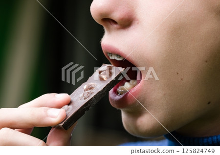 Child eating a piece of chocolate with nuts. Child eating a piece of chocolate with nuts. 125824749