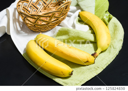 Ripe yellow bananas on a green and white cloth with a wicker basket. 125824830