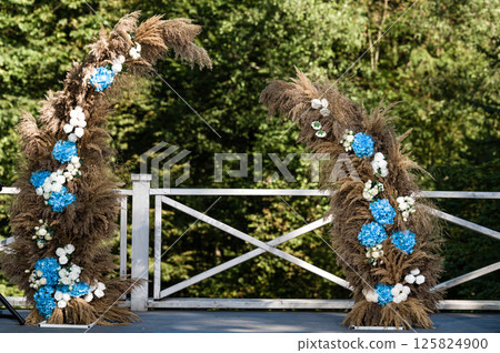Elegant floral wedding arch setup outdoors. Pampas grass and blue hydrangeas create a romantic backdrop. 125824900
