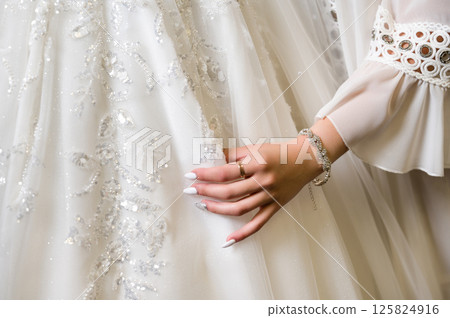 Close-up of a hand delicately touching a white, embellished wedding gown. Sparkling details and elegant design. 125824916