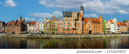 Panoramic view of colorful historic buildings along the Motlawa River in Gdansk, Poland. Features vibrant architecture with a backdrop of blue sky and scattered clouds 125824955