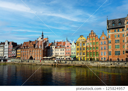 Charming historic architecture lines the waterfront of Gdansk under a clear blue sky. The river is bustling with boats, offering a vibrant scene with the city's iconic brick buildings Charming historic architecture lines the waterfront of Gdansk under a clear blue sky. The river is bustling with boats, offering a vibrant scene with the city's iconic brick buildings 125824957