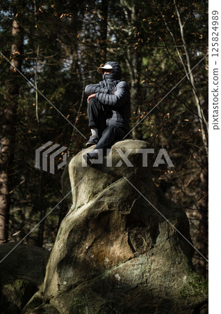 Person sits atop a rock in a forest, contemplating the scenery. Peaceful and serene atmosphere. Person sits atop a rock in a forest, contemplating the scenery. Peaceful and serene atmosphere. 125824989