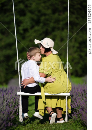 Tender moment: A mother lovingly kisses her son on a swing amidst a lavender field. Tender moment: A mother lovingly kisses her son on a swing amidst a lavender field. 125824993