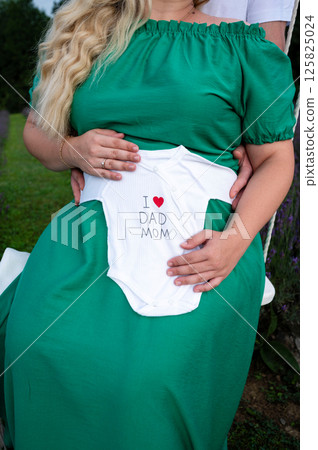 Expecting parents gently hold a baby onesie on mom's belly, a tender moment of anticipation and love. Expecting parents gently hold a baby onesie on mom's belly, a tender moment of anticipation and love. 125825024