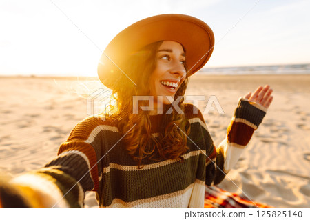Young woman taking a cheerful selfie on a sandy beach during sunset. Lifestyle, travel, active life Young woman taking a cheerful selfie on a sandy beach during sunset. Lifestyle, travel, active life 125825140
