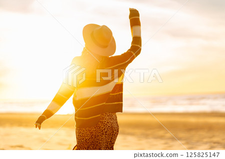 Young woman enjoying sunset at beach while wearing cozy striped sweater. Relax and lifestyle concept Young woman enjoying sunset at beach while wearing cozy striped sweater. Relax and lifestyle concept 125825147