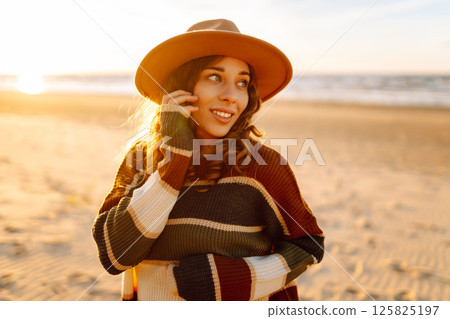 Young woman enjoying sunset at beach while wearing cozy striped sweater. Relax and lifestyle concept 125825197