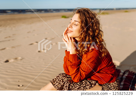 Portrait of curly woman on beach in cold sunny weather. Travel, weekend, relax and lifestyle concept Portrait of curly woman on beach in cold sunny weather. Travel, weekend, relax and lifestyle concept 125825229