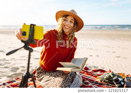 Young woman recording video using smartphone on tripod on the seashore. Travel, blogging concept. Young woman recording video using smartphone on tripod on the seashore. Travel, blogging concept. 125825317