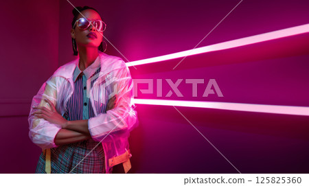 Stylish y2k woman in translucent jacket and sunglasses with pink overhead neon tube 125825360