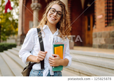 Woman student holds several colorful notebooks, standing outside university. University Student. Woman student holds several colorful notebooks, standing outside university. University Student. 125825878