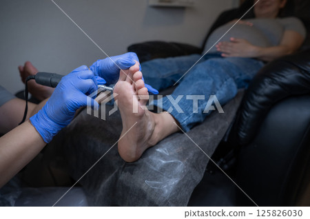 Pregnant woman on a hardware pedicure procedure in a beauty salon. Pregnant woman on a hardware pedicure procedure in a beauty salon. 125826030