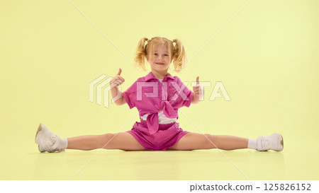 Happy girl child in pink summer clothes and ponytail hairstyle sitting on twine on floor, giving thumbs up and smiling Happy girl child in pink summer clothes and ponytail hairstyle sitting on twine on floor, giving thumbs up and smiling 125826152