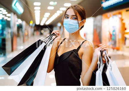 Fashionable woman in protective medical mask with shopping bags walking in the mall. Covid-19. Fashionable woman in protective medical mask with shopping bags walking in the mall. Covid-19. 125826160