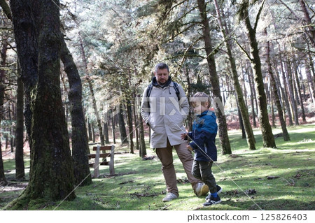 Father and son hiking in sunny forest, enjoying nature walk 125826403
