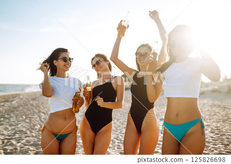 Happy Four girls dancing and drinking beers on the beach at sunset. Summer holidays, vacation. 125826698