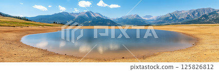 serene lake surrounded by mountains on sunny day, reflecting sky 125826812