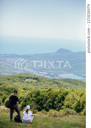 Two tourists looking at the green forest from the top of the mountain Two tourists looking at the green forest from the top of the mountain 125826974