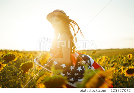Beautiful girl in hat with the American flag in a sunflower field. 4th of July. Fourth of July. Freedom Beautiful girl in hat with the American flag in a sunflower field. 4th of July. Fourth of July. Freedom 125827072