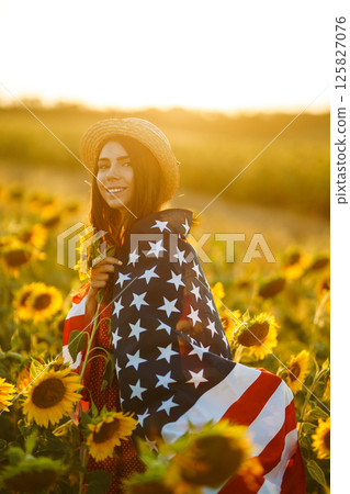 Beautiful girl in hat with the American flag in a sunflower field. 4th of July. Fourth of July. Independence Day. 125827076