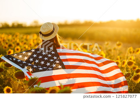 Beautiful girl in hat with the American flag in a sunflower field. 4th of July. Fourth of July. Independence Day. Beautiful girl in hat with the American flag in a sunflower field. 4th of July. Fourth of July. Independence Day. 125827077