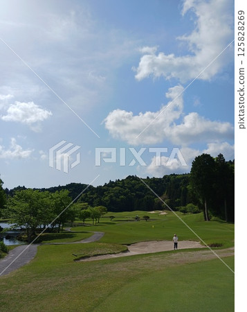 A sunny day at a golf course and a golfer standing in a bunker 125828269