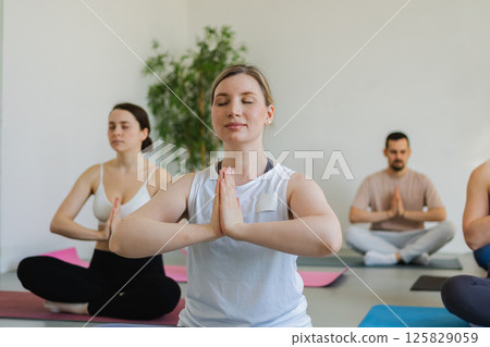 Yoga mindfulness meditation. Group of sporty people doing exercise in studio for class for yoga wellness mindfulness meditation. Men women practicing yoga sitting in lotus pose meditating relaxing 125829059