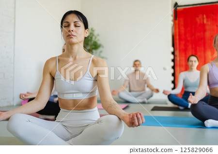 Yoga mindfulness meditation. Group of sporty people doing exercise in studio for class for yoga wellness mindfulness meditation. Men women practicing yoga sitting in lotus pose meditating relaxing Yoga mindfulness meditation. Group of sporty people doing exercise in studio for class for yoga wellness mindfulness meditation. Men women practicing yoga sitting in lotus pose meditating relaxing 125829066