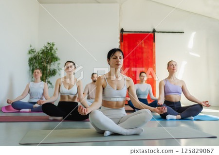 Yoga mindfulness meditation. Group of sporty people doing exercise in studio for class for yoga wellness mindfulness meditation. Men women practicing yoga sitting in lotus pose meditating relaxing Yoga mindfulness meditation. Group of sporty people doing exercise in studio for class for yoga wellness mindfulness meditation. Men women practicing yoga sitting in lotus pose meditating relaxing 125829067