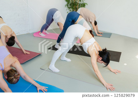 Yoga class Pilates workout. Group of sporty people doing exercise in studio class for yoga wellness mindfulness meditation. Personal trainer men women practicing yoga in gym training stretching indoor Yoga class Pilates workout. Group of sporty people doing exercise in studio class for yoga wellness mindfulness meditation. Personal trainer men women practicing yoga in gym training stretching indoor 125829079
