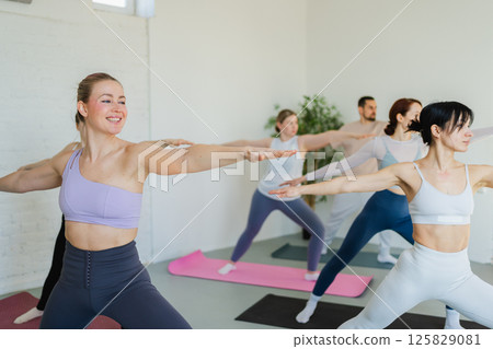 Yoga class Pilates workout. Group of sporty people doing exercise in studio class for yoga wellness mindfulness meditation. Personal trainer men women practicing yoga in gym training stretching indoor 125829081