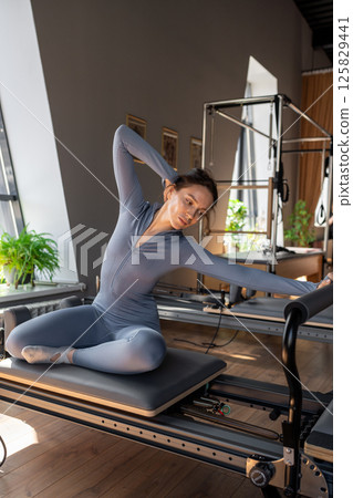 Woman doing mermaid exercise in a sunlite, modern pilates studio, embodying calm, focus, and strength. 125829441