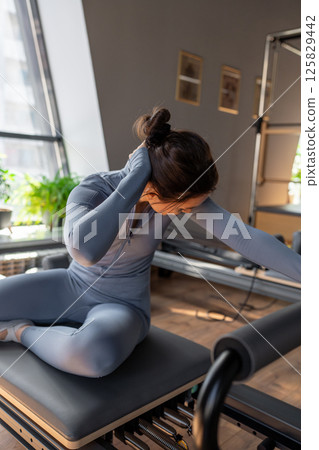 Woman doing mermaid exercise in a sunlite, modern pilates studio, embodying calm, focus, and strength. 125829442