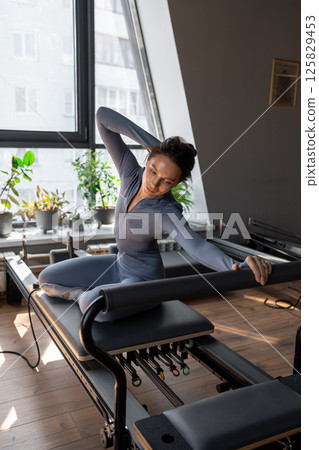 Woman doing mermaid exercise in a sunlite, modern pilates studio, embodying calm, focus, and strength. 125829453