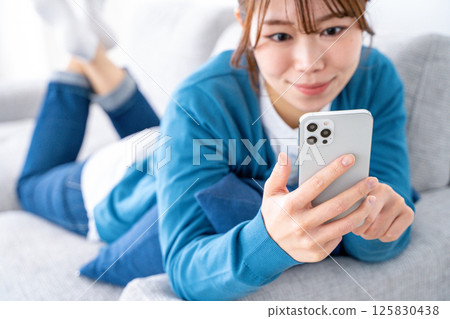 A woman watching a smartphone on a sofa 125830438