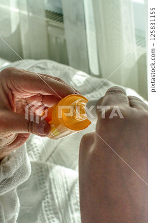 female Hands opening orange skincare serum bottle in cozy morning light on white bed. High quality photo 125831155