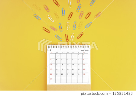 May 2026 desk calendar and paper clips on yellow background. 125831483