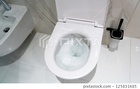 A white modern toilet flushing clean water in a hygienic bathroom setting 125831685