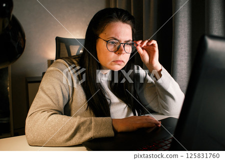 Young freelance accountant working remotely on laptop at home. Managing finances of business. Calculating incomes and expenses. Focusing on process. 125831760