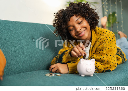 Saving money investment for future. African American girl putting money coin in pink piggy bank. Saving investment budget business wealth retirement financial money banking concept 125831860