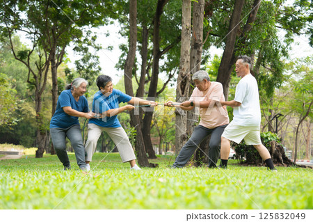Four cheerful seniors in a friendly tug of war on a vibrant green lawn showcasing their vitality, camaraderie, and Active Seniors lifestyle, enjoying an active and playful moment in a park setting. 125832049