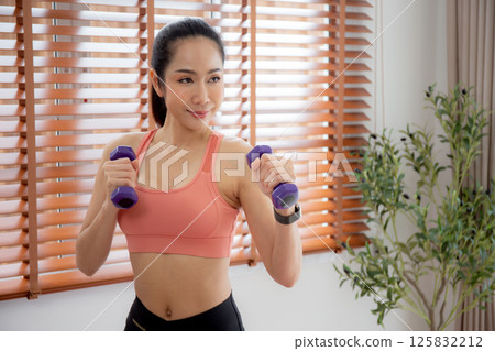 Young asian woman in sportswear workout with dumbbells for strength and strong in living room. Young asian woman in sportswear workout with dumbbells for strength and strong in living room. 125832212