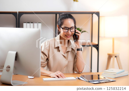 Young asian business woman using desktop computer while talking with smart phone. 125832214