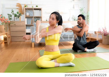 Young asian couple practicing yoga in living room at home, stretching arm pose. 125832229