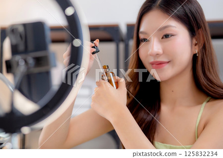 Young asian woman demonstrating serum on hands on social media at home. 125832234