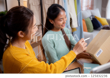 Two young asian woman working while planning online business and checking order with writing. Two young asian woman working while planning online business and checking order with writing. 125832236