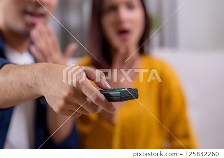 Happy couple relax sitting on sofa while a dramatic TV show in living room at home. 125832260