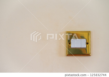 Triple light switch. Gold switch with white details and magnolia wall. All switches in off position. No branding. Copy space to left. Triple light switch. Gold switch with white details and magnolia wall. All switches in off position. No branding. Copy space to left. 125832744